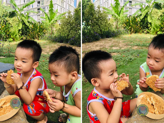 Bé vui vẻ cầm gói cơm cháy Cô Ba tại bàn ăn trong gian bếp gia đình